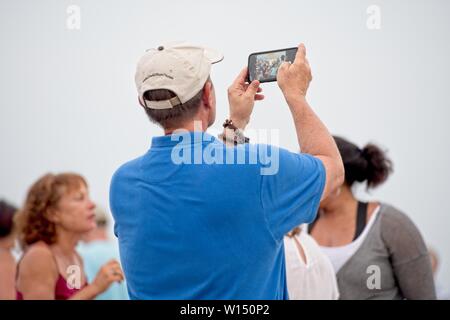 A man holds up his smart phone to take a selfie with the people that are standing behind him. Stock Photo