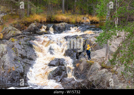 Tourist with a backpack looking at a waterfall in a park in a beautiful autumn nature landscape. Portrait of adult woman back standing outdoor. Stock Photo