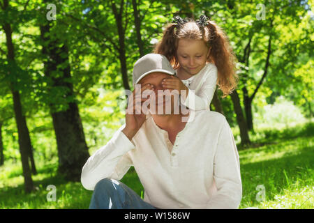 Close up portrait young male with closed eyes indoors. Happy cheerful little daughter playing covering daddy eyes with hands prepare for him surprise Stock Photo