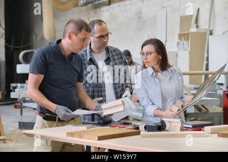 Group of industrial people client, designer or engineer and workers working together on project of wooden furniture. Teamwork in carpentry workshop. Stock Photo