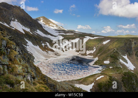 Beautiful, framed, sunlit view from Lakes peak on Rila mountain on The Eye lake, one of famous seven Rila lakes, still covered by broken ice in June Stock Photo