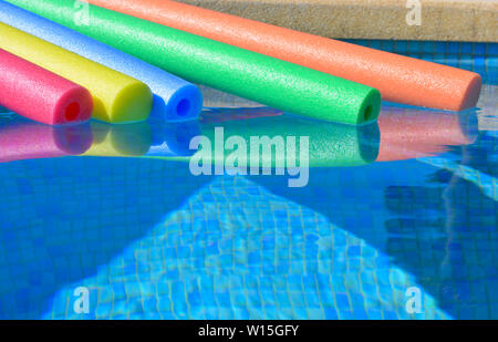 Brightly coloured pool noodles and swimming pool, with copy space. Fun summer vibes. Stock Photo