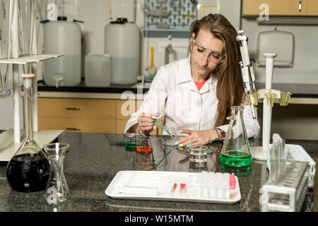 Young, Caucasian white, female laboratory technician in white robe sampling with pipette chemical liquid solution in laboratory, lab equipment and gla Stock Photo