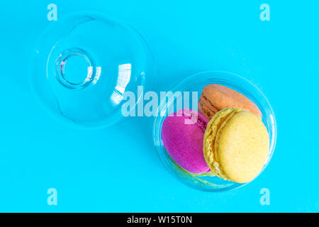 Flat lay of colorful macaroons in glass bowl against blue background minimal creative sweet food concept. Stock Photo