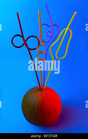 bright colored cocktail tubes stuck in a melon on a blue background Stock Photo