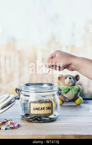 Selective focus on child hand, put euro coin in swear jar. Every time child curses or swears it has to put money as punishment in jar for safe keeps. Stock Photo