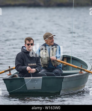 Young man 20 years old and grandad 75 years fishing for trout from boat on Scottish loch. Stock Photo