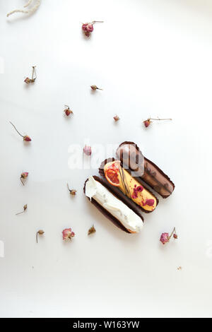 Set of three eclairs with different fillings and design. Isolate on a white surface decorated with dry roses, copyspace Stock Photo