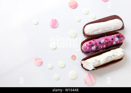 A set of three eclairs with different fillings and design isolate on a white surface decorated with drops of white chocolate, copyspace Stock Photo