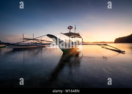 Tropical harbor bay in evening. Golden hour in lagoon in Philippines, Palawan, El Nido. Sunset on beach. Tranquil scenic sundown above mountains Stock Photo