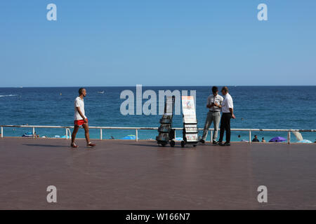 Man passing Jehovah's Witnesses who are distributing illustrated religious magazines on Promenade des Anglais in Nice, France Stock Photo