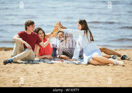 Full length portrait of group of friends enjoying picnic on beach in Summer, copy space Stock Photo