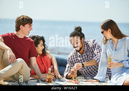 Portrait of group of friends enjoying picnic on beach in Summer, copy space Stock Photo