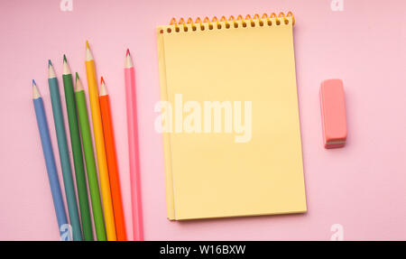 Blank page of vertical spiral sketching pad with crayons on pink background, flat lay. Back to school. Stock Photo