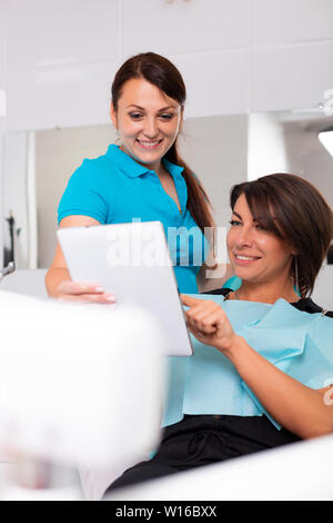 Female dentist showing teeth x-ray on digital tablet screen. Patient sitting on chair in professional dental clinic Stock Photo