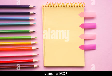 Blank page of vertical spiral sketching pad with crayons on pink background, flat lay. Back to school. Stock Photo