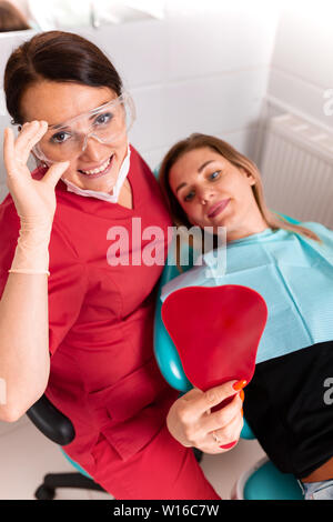 The dentist and her happy patient look at the camera and smile. Reception at the dentist, healthy teeth, happy patient, beautiful teeth. Stock Photo