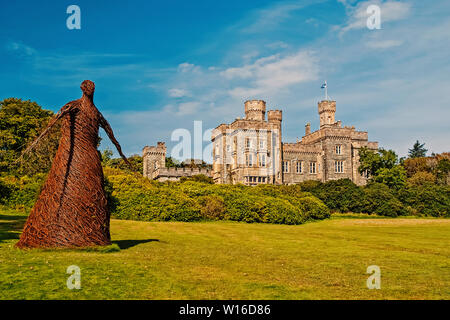 Wicker woman statue and castle in Stornoway, United Kingdom. Willow sculpture on green grounds of Lews Castle estate. Architecture and design. Landmark and attraction. Summer vacation and wanderlust.