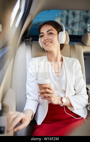 Portrait of young businesswoman listening to music in taxi and smiling happily Stock Photo