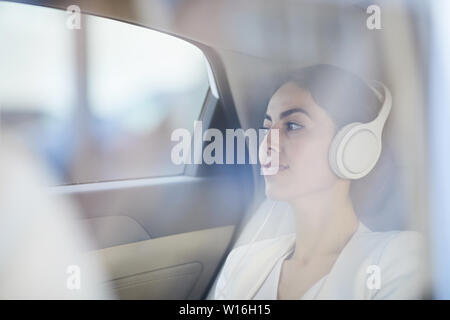 Side view portrait of young businesswoman listening to music in taxi shot from behind glass, copy space Stock Photo