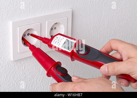 Male electrician measuring power on wall outlet with measuring device - close up with selective focus Stock Photo