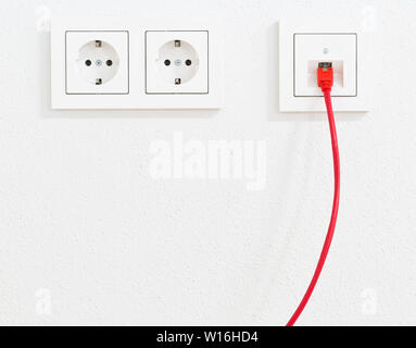 Red network cable in wall outlet for office or private home lan ethernet connection with power outlets flat view on white plaster wall background Stock Photo