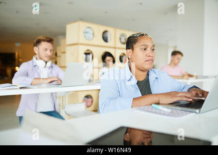 Serious busy young interracial entrepreneurs sitting in co-working space and using modern laptops while working with data Stock Photo