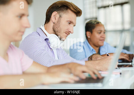 Serious concentrated hipster guy with stubble sitting at table and making notes in notepad while analyzing information Stock Photo