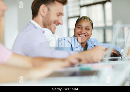 Jolly carefree young multi-ethnic student friends sitting at one table and chatting together while doing task in library Stock Photo