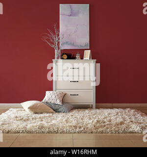 Chest of drawers with stylish decor and pillows near color wall in room Stock Photo