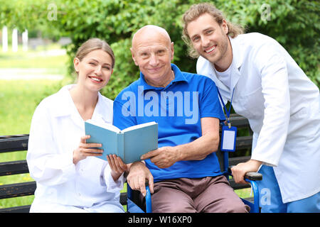 Elderly man with caregivers reading book in park Stock Photo