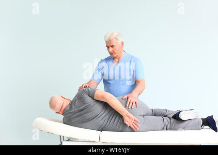 Mature physiotherapist working with senior man on light background Stock Photo