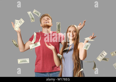 Happy couple with falling dollar banknotes on grey background Stock Photo