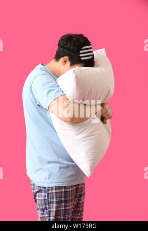 Handsome young man with sleep mask and pillow on color background Stock Photo