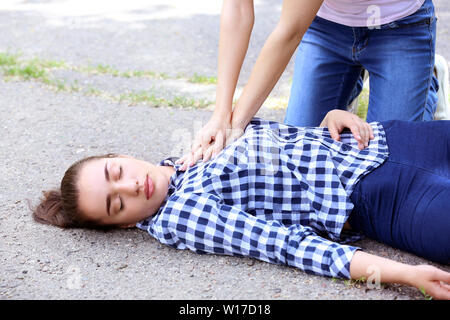 Female passer-by doing CPR on unconscious woman outdoors Stock Photo