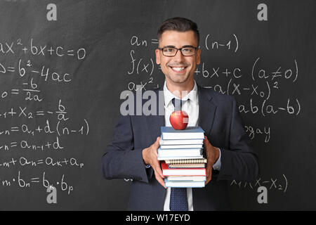 Handsome math teacher with books near blackboard in classroom Stock Photo