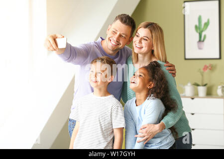 Happy couple with little adopted children taking selfie at home Stock Photo