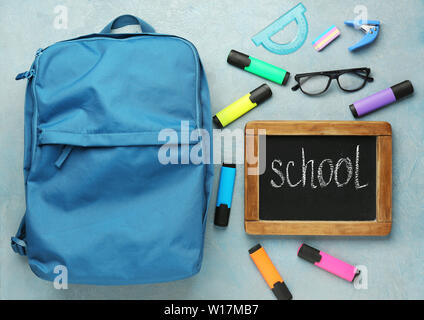 Backpack with supplies and chalkboard with word SCHOOL on grey background Stock Photo