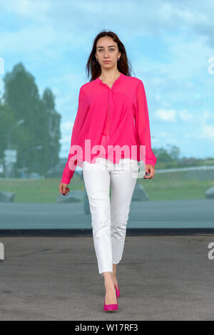 Elegant young woman in pink stilettos with matching top walking in front of large windows Stock Photo