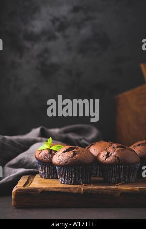 Chocolate Muffins In Paper Cups On A Wooden Board, Black Background. Vertical Still Life Composition. Copy Space Stock Photo