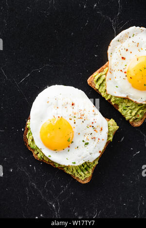 Breakfast sandwich with fried egg and avocado on toasted bread. Black marble background. Top view Stock Photo