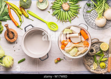 Cooking pot with spoon and white colander with fresh vegetables for vegetarian stock , broth or stew  in light kitchen table background, top view.  Co Stock Photo