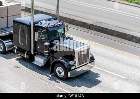 Black stylish powerful big rig classic industrial semi truck with chrome accessories and vertical exhaust pipes transporting cargo on flat bed semi tr Stock Photo