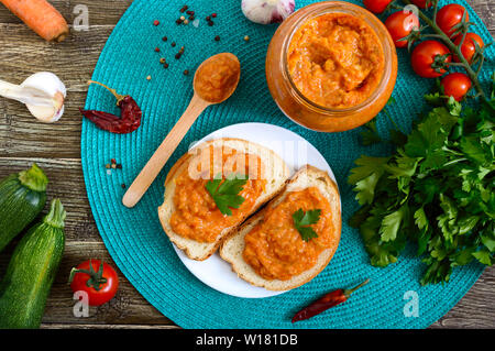 Delicious squash caviar in a jar and spread on slices of white bread on the table. Homemade caviar with zucchini, garlic, carrots, tomato sauce. Vegan Stock Photo