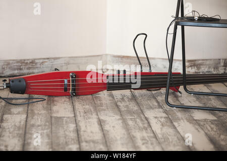 Live music background, modern electric red double bass lays on grungy wooden floor of musical studio, close-up photo with selective focus Stock Photo