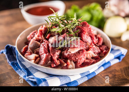 Raw beef pieces with rosemary in bowl on butcher board Stock Photo