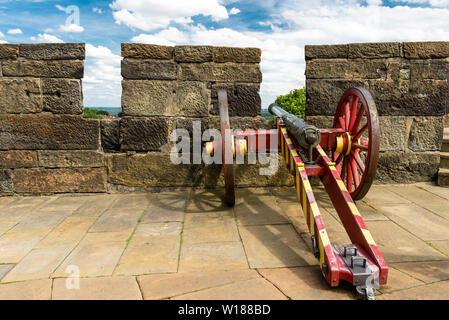 An antique cannon in red-yellow color on the walls of a medieval castle. Stock Photo