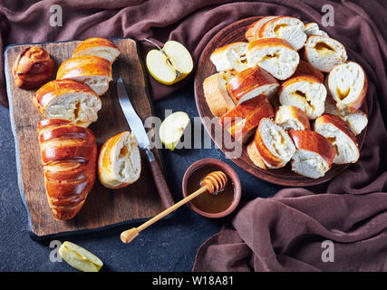overhead view of freshly baked sweet rolls with Apple jam filling on an earthenware plate on a kitchen rustic wooden table with honey in bowl, horizon Stock Photo