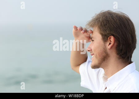 Happy man scouting looking away on the beach with hand on forehead Stock Photo