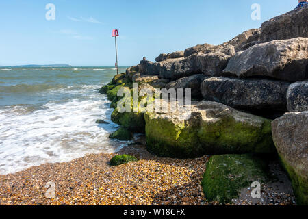 A groyne made of large boulders on Avon Beach at Mudeford, Christchurch in Dorset, UK with blue sky on a hot, sunny, summer day, Stock Photo